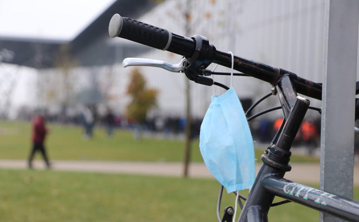 Una mascarilla en el manillar de una bicicleta frente al Palacio de Exposiciones con cola para recibir la tercera dosis de la vacuna.