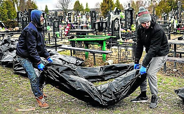 Oficiales de Policía y forenses transportan cuerpos que alinean en el cementerio de Bucha, donde se realiza el proceso de registro antes de su inhumación. 