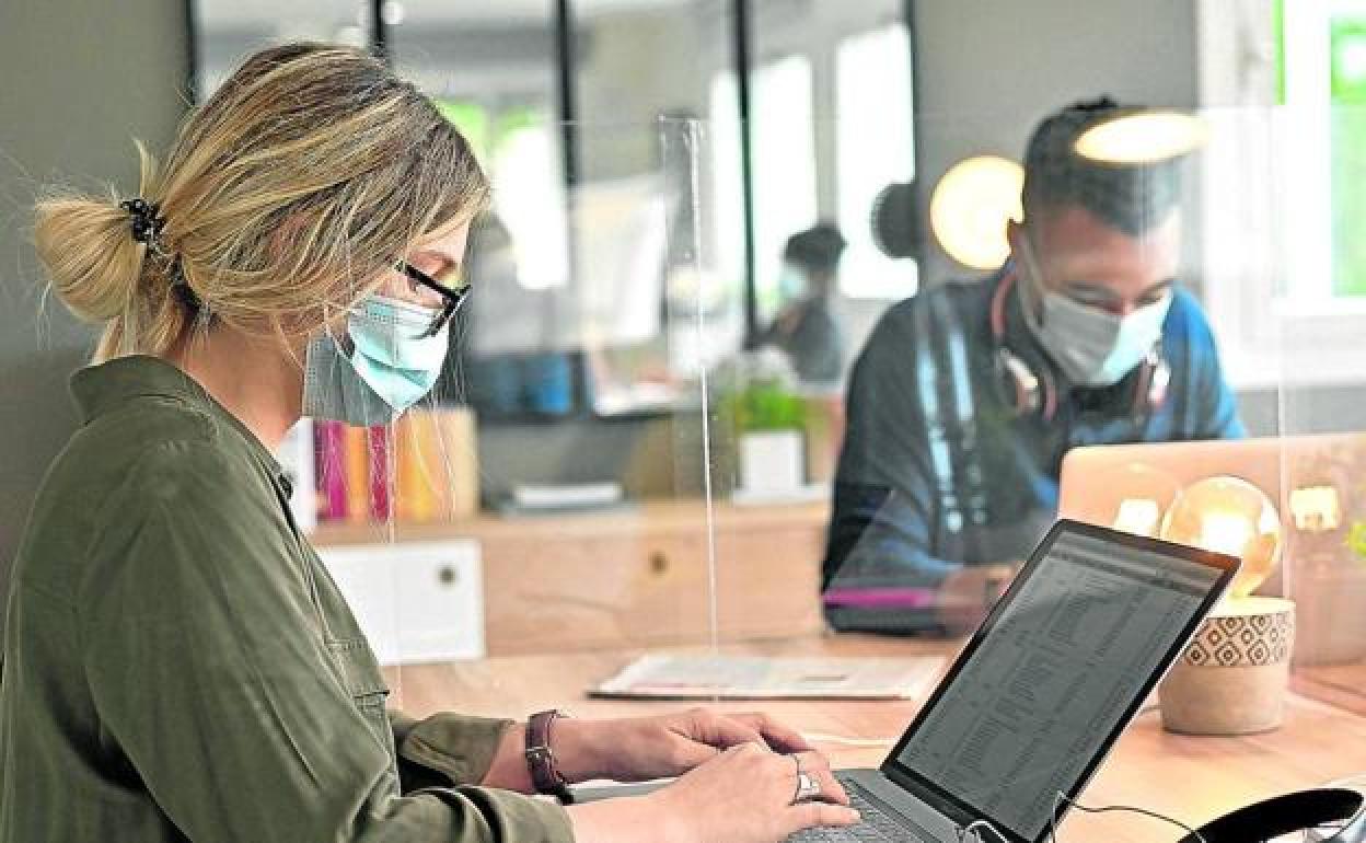 Imagen de archivo de una trabajadora con mascarilla en su puesto de trabajo. 