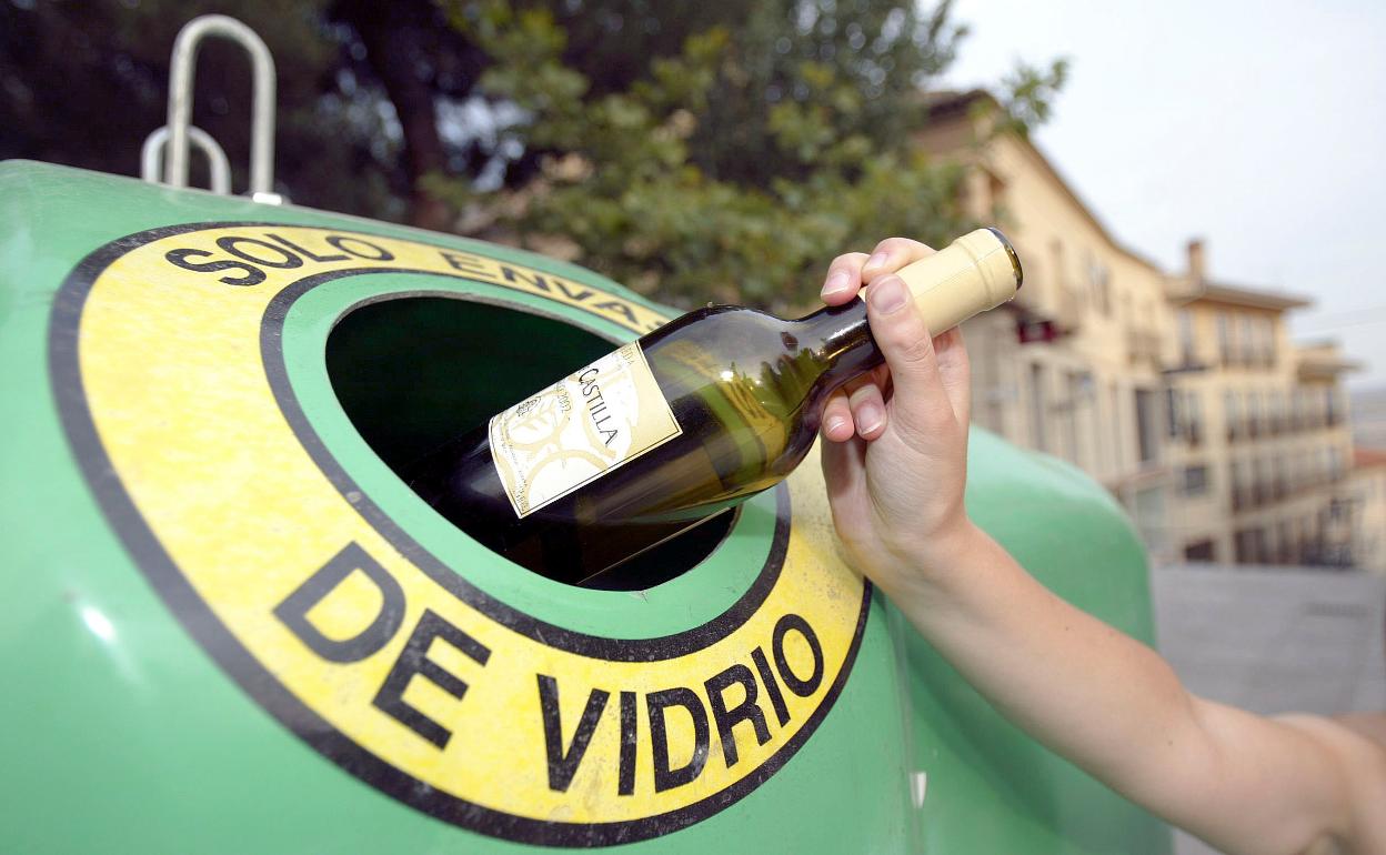 Una mujer recicla una botella de vino en un contenedor de vidrio. 