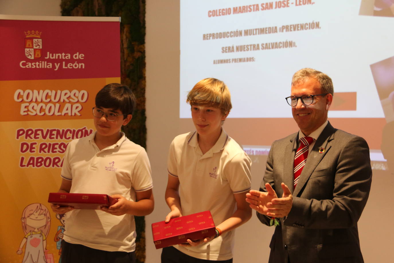 El consejero de Industria, Comercio y Empleo, Mariano Veganzones, entrega a los alumnos de primaria Manuel Cortés y Jorge González de Paz de este colegio leonés el galardón por su vídeo en el que repasan la importancia de prevenir en el colegio yen el trabajo para mejorar la seguridad.