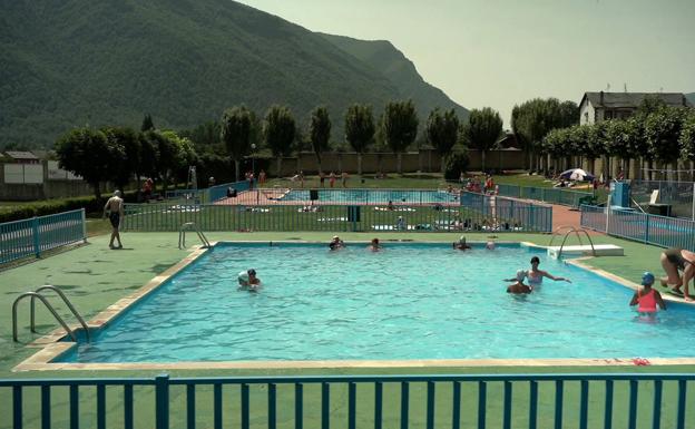 Un grupo de bañistas se refrescan en las piscinas de Villablino con la montaña de fondo. 