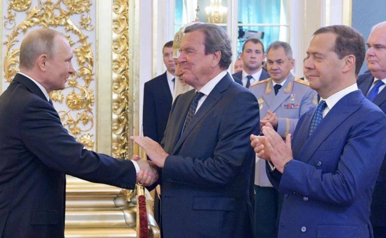 Vladímir Putin estrecha la mano del excanciller y líder socialdemócrata alemán Gerhard Schröeder en presencia del primer ministro ruso Dmitry Medvedev en 2018