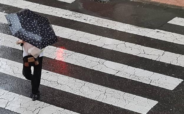 Una mujer cruza un paso de peatones bajo la lluvia en León el lunes 29 de agosto.