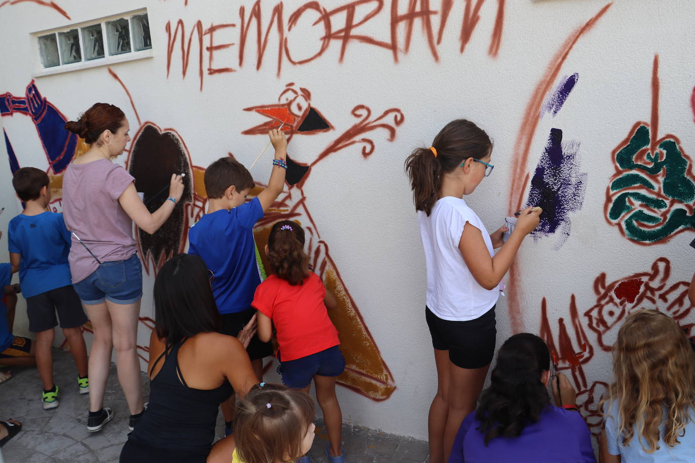 Laia supervisa y ayuda a los más jóvenes para pintar el mural