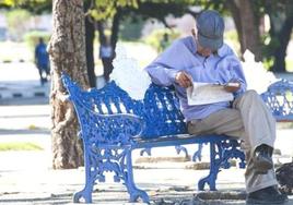 Un pensionista lee el periódico en un banco.