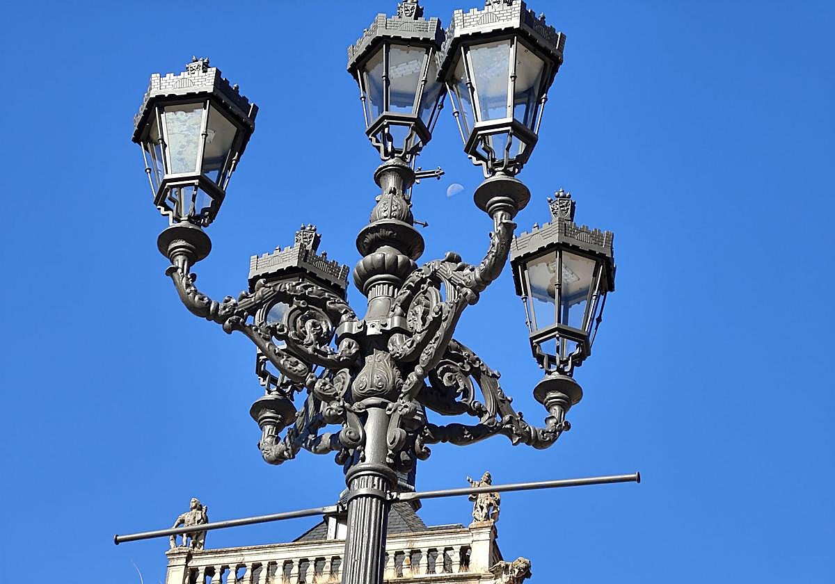 La luna vista entre los brazos de una farola de la Plaza Mayor de León.