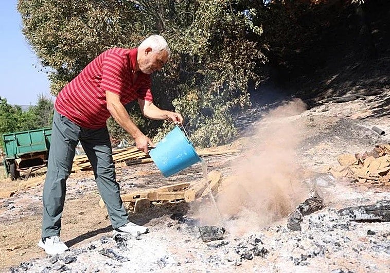 Un vecino de Palacios de Jamuz echa agua a un resquicio del fuego, que todavía ardía este viernes.
