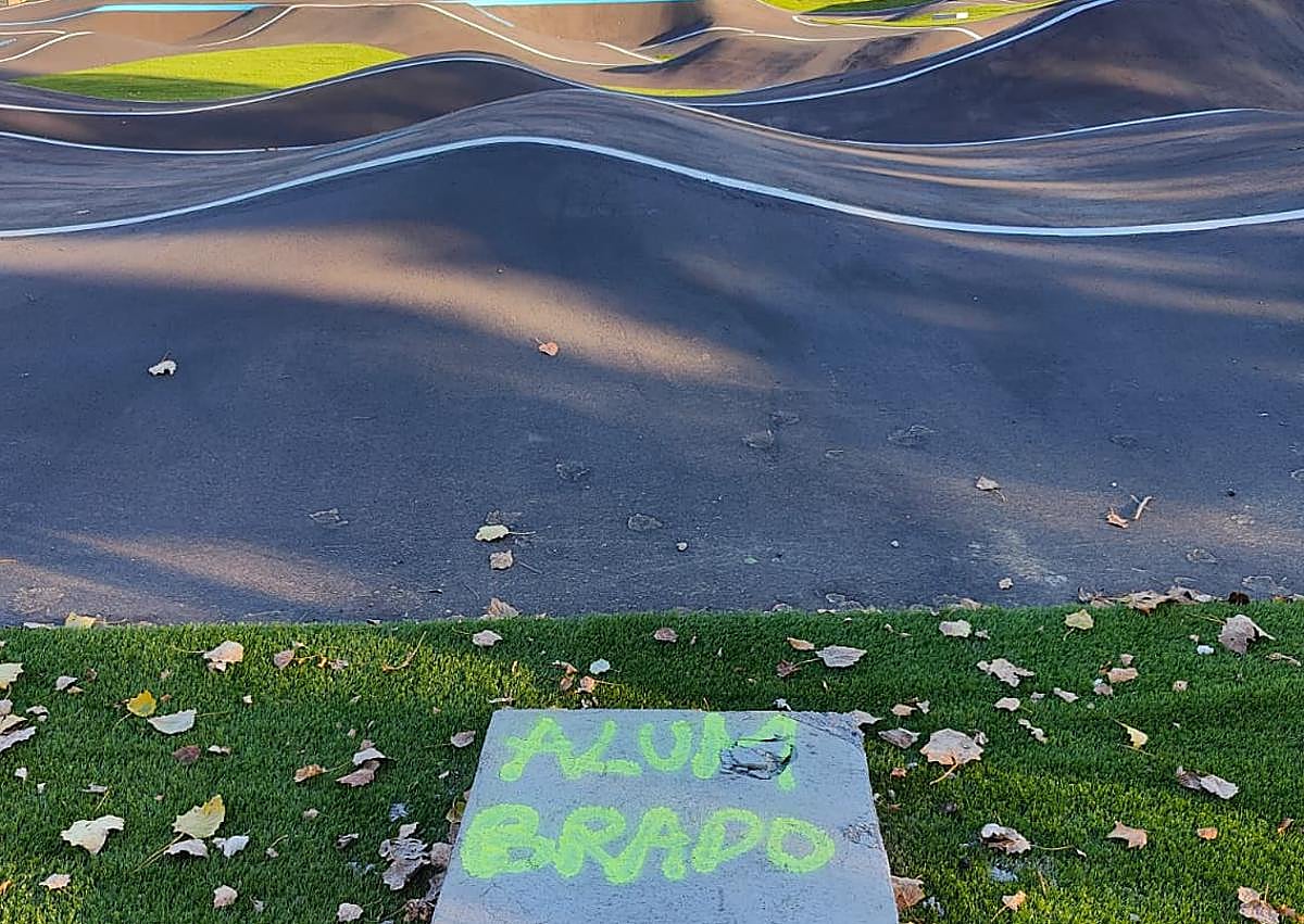 Imagen secundaria 1 - Cartel con las obligaciones de los usuarios; marca que anuncia la colocación de un dispositivo de alumbrado; y una flecha roja que indica la dirección y la dificultad -avanzada- de esta parte de la pista de pumptrack en Puente Castro.