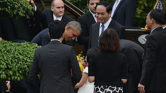 Obama recibe flores de una niña mientras el presidente Tran Dai Quang observa la escena.