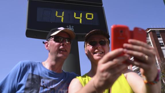 Dos turistas se hacen una foto con el termómetro que marca 44º en Córdoba.