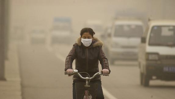 Joven china, protegida por una mascarilla, circula en bicicleta por una calle de Lanzhou, ciudad que sufre unos niveles altos de contaminación.