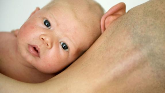 Un padre sostiene contra su cuerpo a su bebé de cuatro semanas.