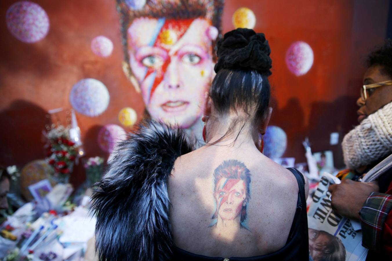 Una joven con la espalda tatuada rinde homenaje a Bowie frente al mural que pintó en Brixton, South London, el artista callejero Jimmy C.