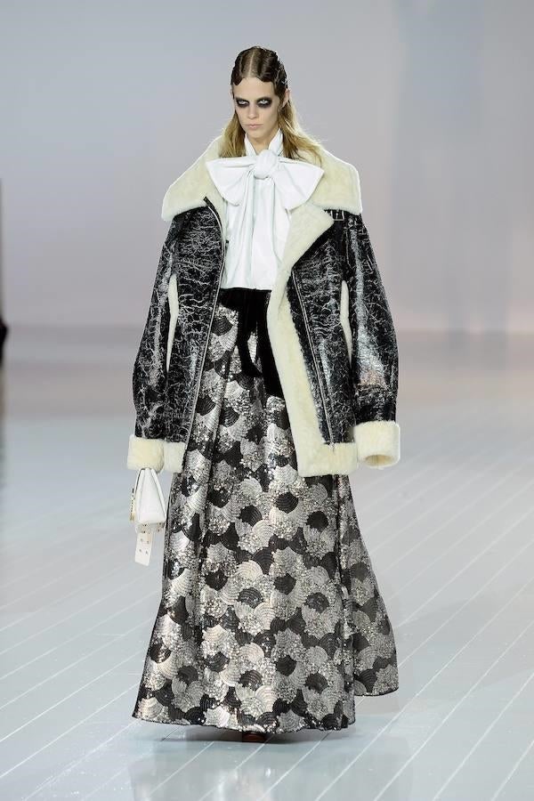 Una extraña combinación: parka de piel blanca y negra, con falda larga plateada y camisa blanca con lazo gigante.