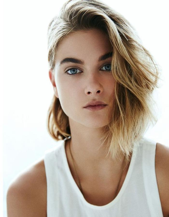 Raíces oscuras con tonos rubios desde medios a puntas en un peinado con raya ladeada y parte retirado del rostro.