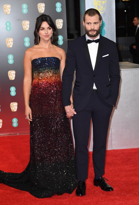 Mientras Jamie Dornan se decantó por un esmoquin, su esposa Amelia Warner apostó por las paillettes en un vestido con escote palabra de honor y degradación de colores arco iris de Ong Oaj.