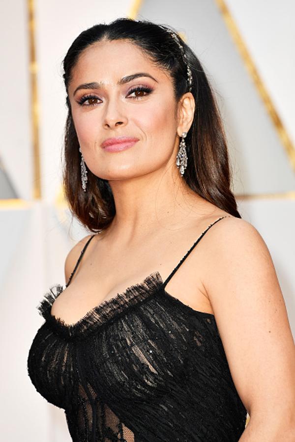 Salma Hayek dejó su melena suelta que adornó con una diadema. En su maquillaje destacan los ojos con sombras rosas, eyeliner marcado y abundante máscara de pestañas, y labios naturales y acabado gloss.