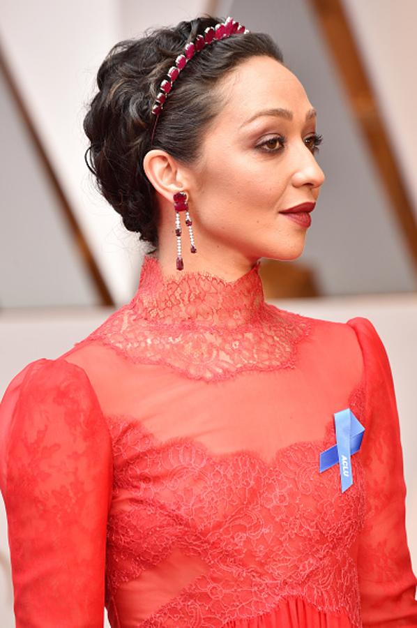Ruth Negga con pixie ondulado con diadema a juego con los pendientes, y labios en burdeos.