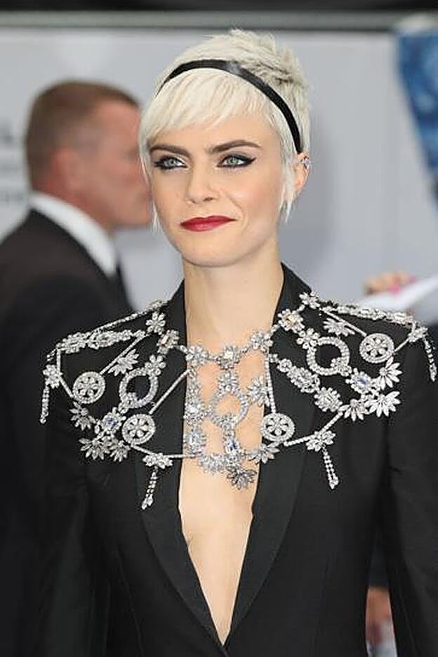 Cara Delevingne lleva pixie con postizos en flequillo y patillas y adornado con una cinta negra en forma de diadema.