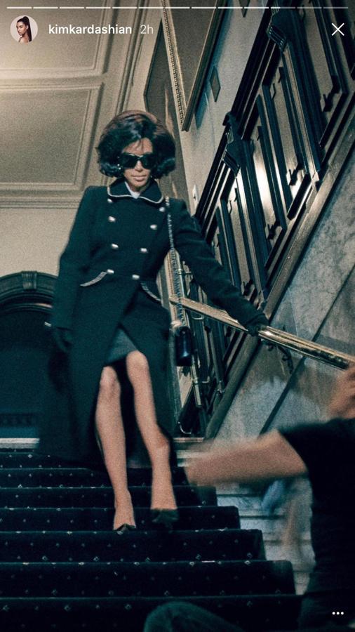 La Kardashian bajando las escaleras de un edificio con un abrigo negro largo y unas gafas de sol.