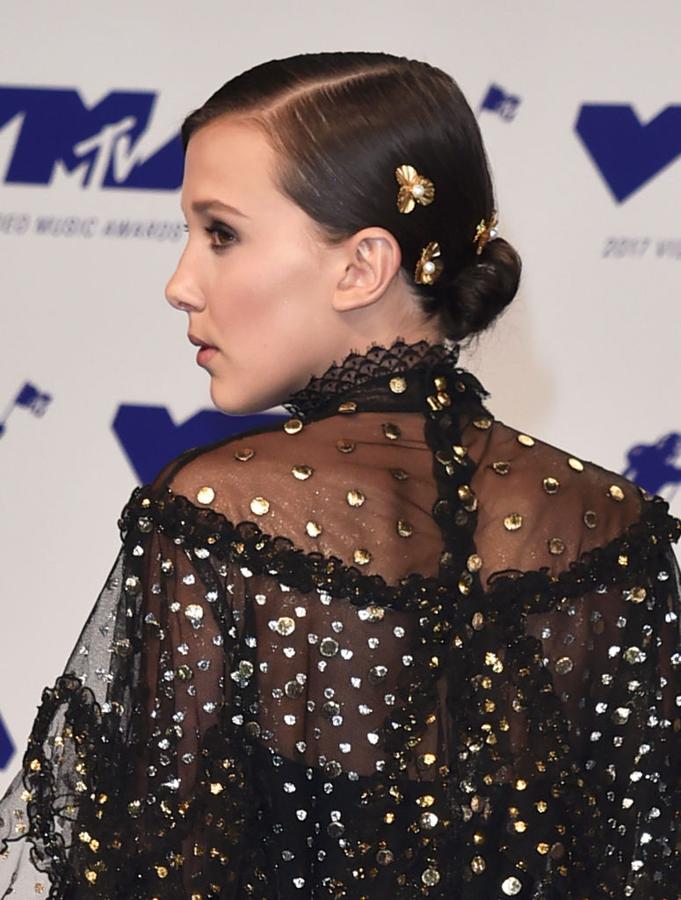 El clásico moño de bailarina, pero a la altura de la nuca y con raya lateral es otro peinado perfecto para tus bodas de otoño. Nos encantan los accesorios dorados que ha elegido la actriz Millie Bobby Brown para adornarlo.