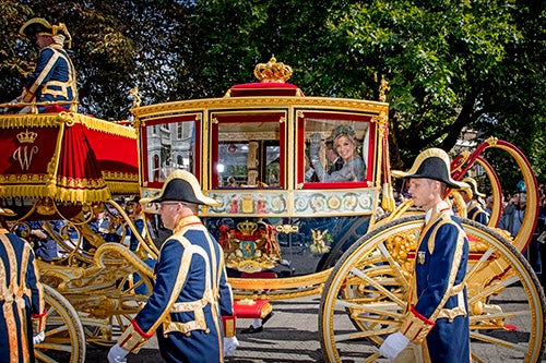 La Reina Máxima y el Rey Willem-Alexander saludando dentro de la carroza con el cuerpo de seguridad fuera de ella.