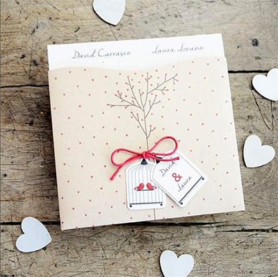 Invitación de boda de tonos amarillentos, simulando cartón y en forma de estucheEn el exteriorunas etiquetas con unos graciosillos pajaros y otra con vuestros nombres unidas por un lazo de cuerda rojo.