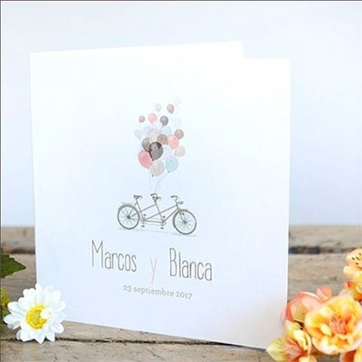 Invitación de boda en forma de díptico con una originales ilustraciones de una bicicleta tandem y unos globos.