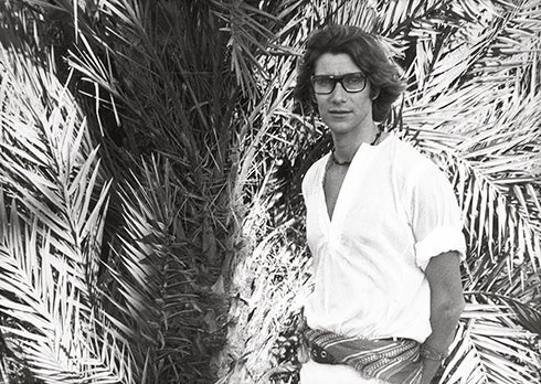 El modisto, Yves Sanit Laurent posando con unas palmeras detrás.