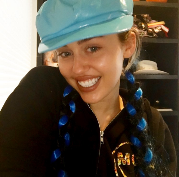 La cantante Miley Cyrus, con unas divertidas trenzas y una gorra marinera de charol en color azul cielo.