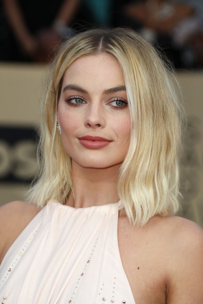 Margot Robbie con el pelo suelto, ondas rotas y raya en el medio y un maquillaje muy luminoso con sombras glitter plateadas y labis rosas con acabado cremoso.