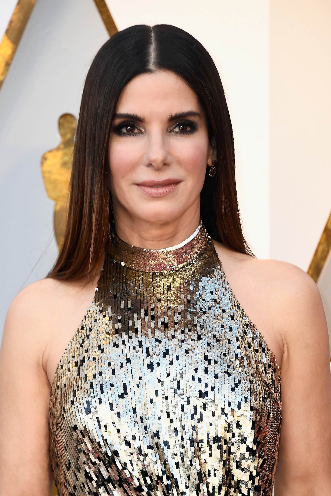 Sandra Bullock con melena suelta lisa con raya en el medio y un bonito maquillaje con sombras doradas y abundante máscara de pestañas.