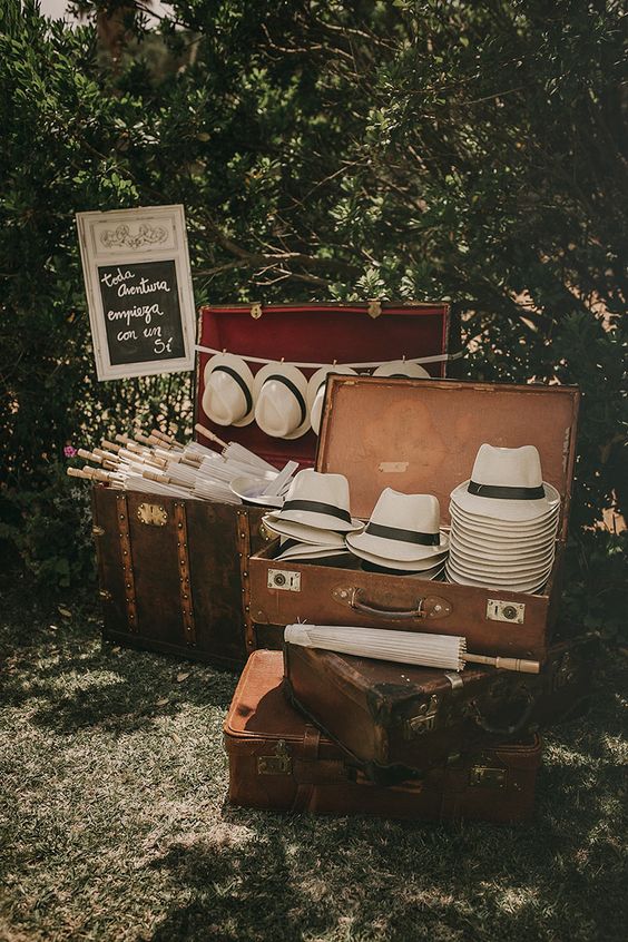 No te olvides de colocar un rincón (este, decorado con  aires viajeros y vintage  es una pasada) donde tus invitados puedan coger sombreros y sombrillas para protegerse del sol.