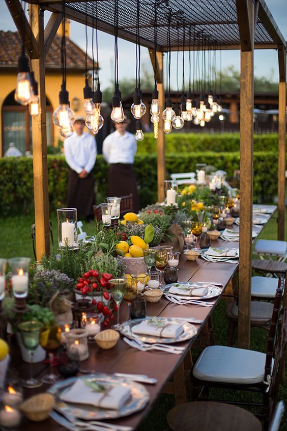 No nos puede gustar más la decoración de estas mesas para boda de verano al aire libre. Los elementos vegetales, el color, la madera vintage y, sobre todo, las luces, crean  un espacio realmente bonito .