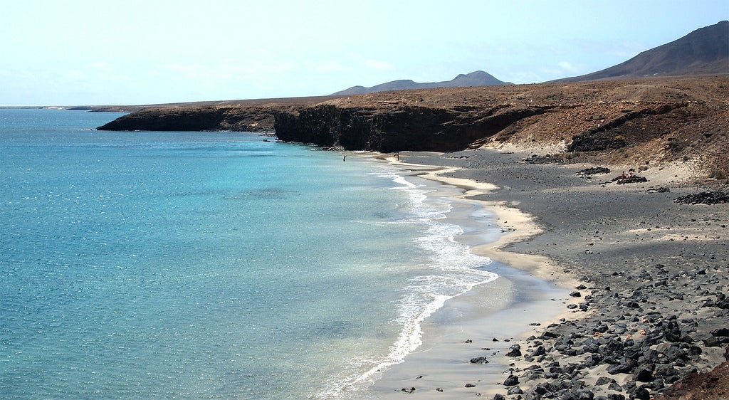 La playa Baja de Juan Gómez la encontramos al sur de Fuerteventura. Desierta y poco turística, podrás disfrutar de unos 400 metros de longitud de arena fina sin nadie a tu alrededor, sobre todo por su difícil acceso. Las piedras que puedes encontrar en alguna de sus partes forman pequeñas piscinas en las que puedes tumbarte y disfrutar del oleaje.