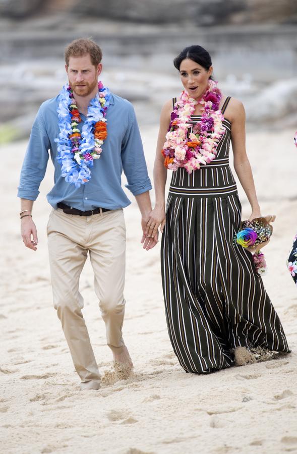 Para su jornada en la playa, Meghan Markle ha apostado por un maxi vestido con estampado de rayas verticales del diseñador australiano Martin Grant, que también firma el trench que está luciendo la Duquesa de Sussex en varias de sus apariciones de este viaje oficial. Lo ha combinado con alpargatas de cuña que no ha dudado en quitarse para caminar por la arena.