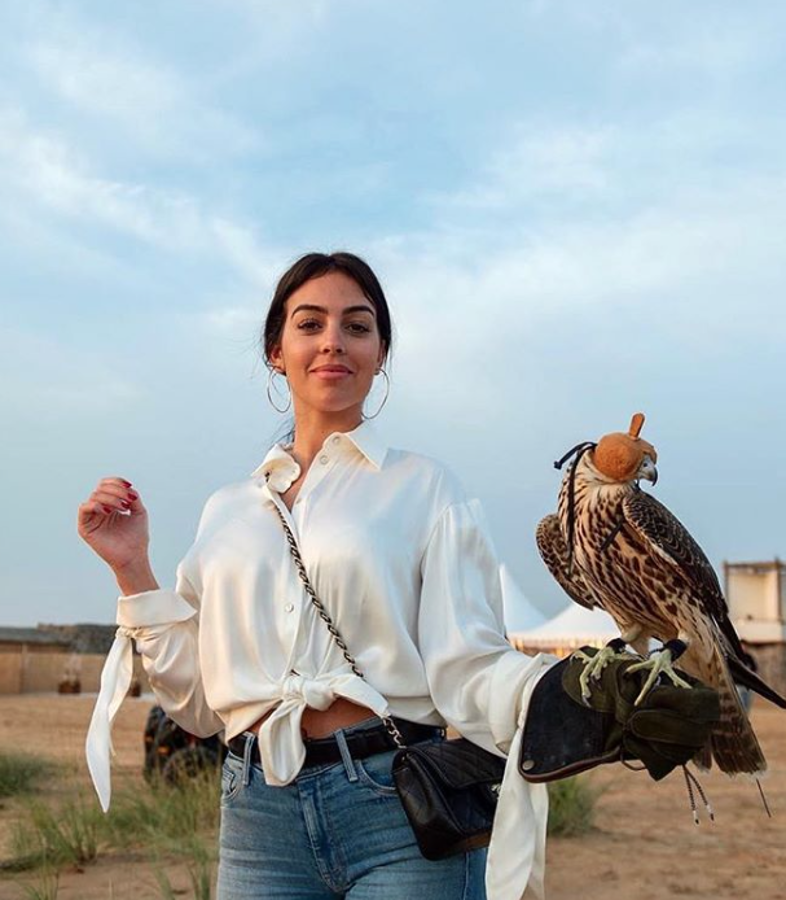 En sus vacaciones de Año Nuevo en Dubai, Georgina Rodríguez visitó en el desierto un safari de cetrería, donde se hizo esta imponente foto. Lleva aquí uno de los estilismos clave de esta temporada: camisa de raso (si es de seda) o de satén (si es de algodón), con ese toque brillante de la lencería tan sugerente; unos "jeans" para romper con su rudeza el lujo de lo satinado; bolso con cadena, como el clásico 2.55 de Chanel y unos aretes XXL. Espectacular.