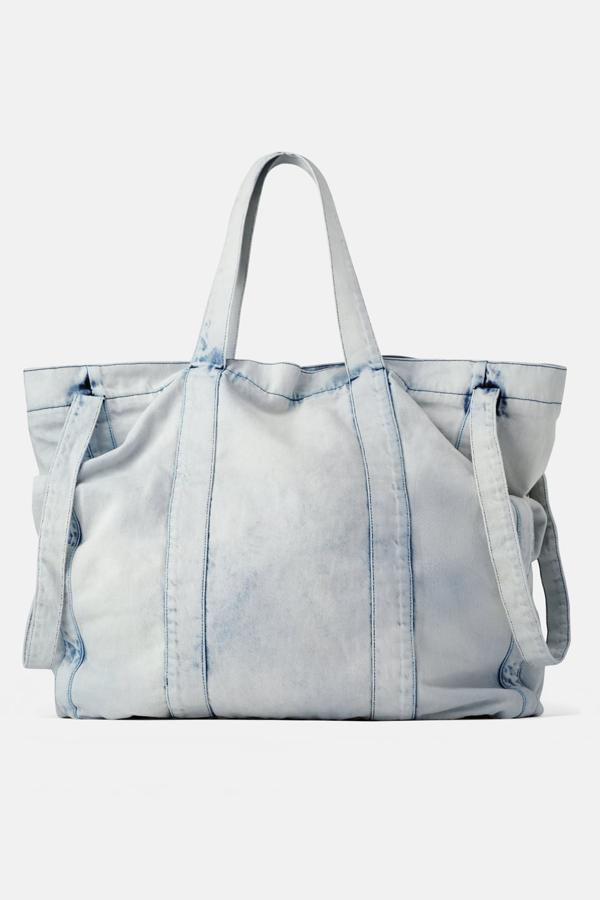 Bolso formato shopper extragrande, de color vaquero desteñido y fabricado con materiales naturales. Lleva un bolsillo en la parte delantera, cuatro asas de hombro multiposición, y dos bolsillo más en el interior, que va forrado. Cierra con cremallera (49,95 euros).