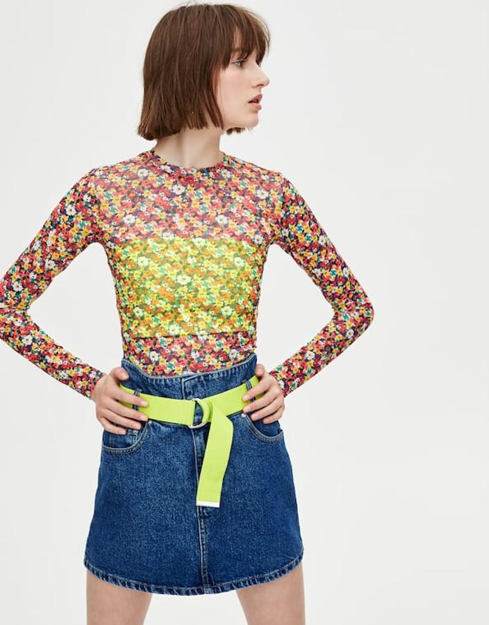 Camiseta de tul de manga larga con cuello redondo, semitransparente y estampado floral (9,99 euros) sobre top 'bandeau' en color flúor y tejido elástico (3,99 euros). Falda vaquera de mujer con cinturilla ancha y cinturón incluido (19,99 euros).