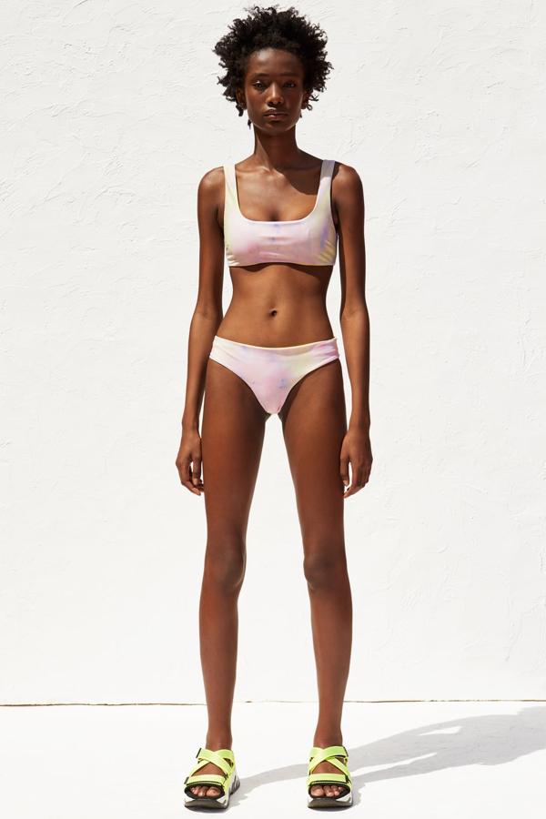 Vemos aquí el reverso del biquini amarillo, en el estampado 'tie dye' en tonos pastel que lleva toda la colección. Las sandalia deportivas de color negro y verde flúor no están fabricadas en materiales reciclados. Llevan tiras cruzadas y una plataforma en relieve que le da a la suela una altura de 5,8 centímetros (35,95 euros).