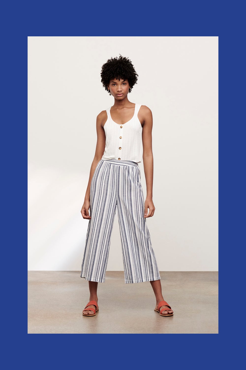 Top de tirantes blanco con botones: 18 euros. Pantalón de pernera ancha a rayas azules: 14 euros. Sandalias trenzadas en color coral: 8 euros. Todo de Primark.