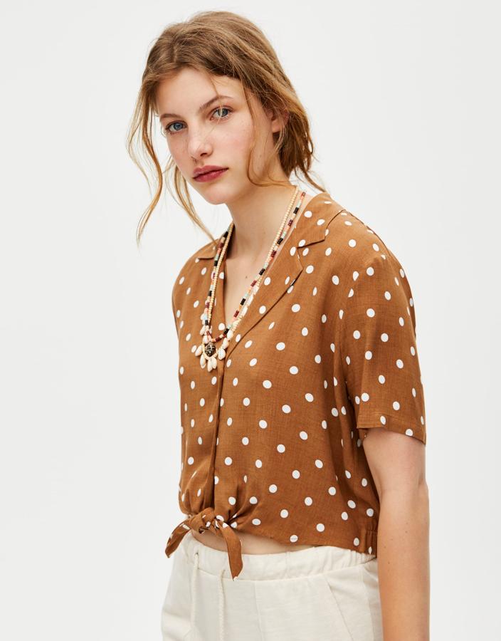 Esta blusa  combina marrón y blanco y lleva un detalle de nudo en la cintura para llevar con pantalones de pinzas y tiro alto en color blanco. Cuesta 15,99 euros.