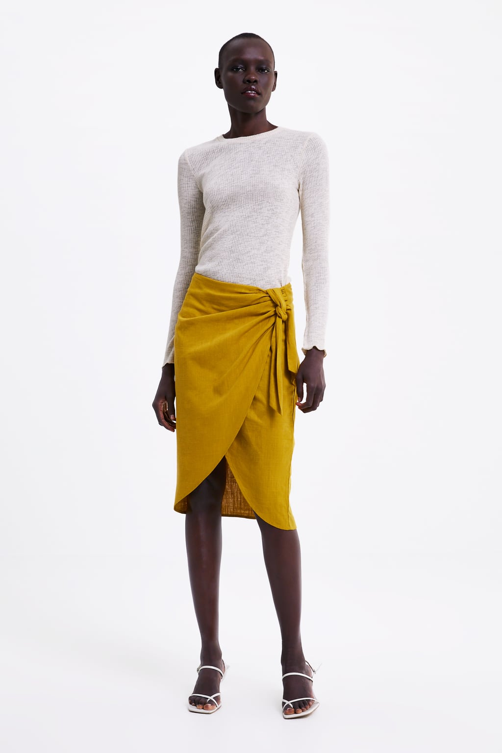 Algunos tejidos como el lino son la opción perfecta para sobrevivir al calor con mucho estilazo, y con esta falda pareo de Zara en tono mostaza vas a triunfar. (25,95 euros).