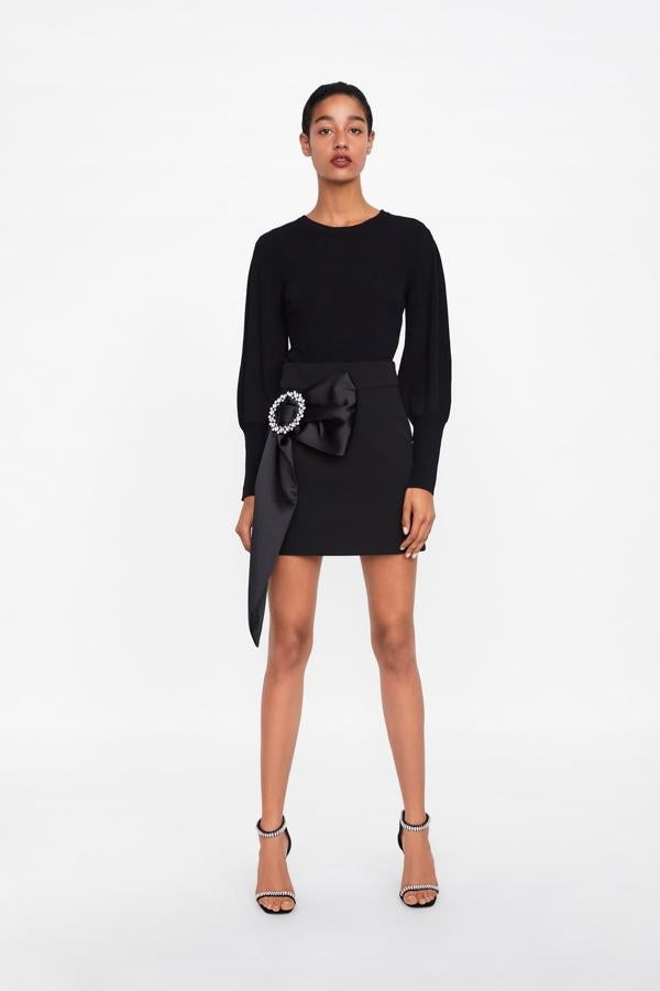 Falda corta con detalle de lazada lateral adornada con una hebilla joya. Cierra con cremallera oculta en costura trasera (49,95 euros).