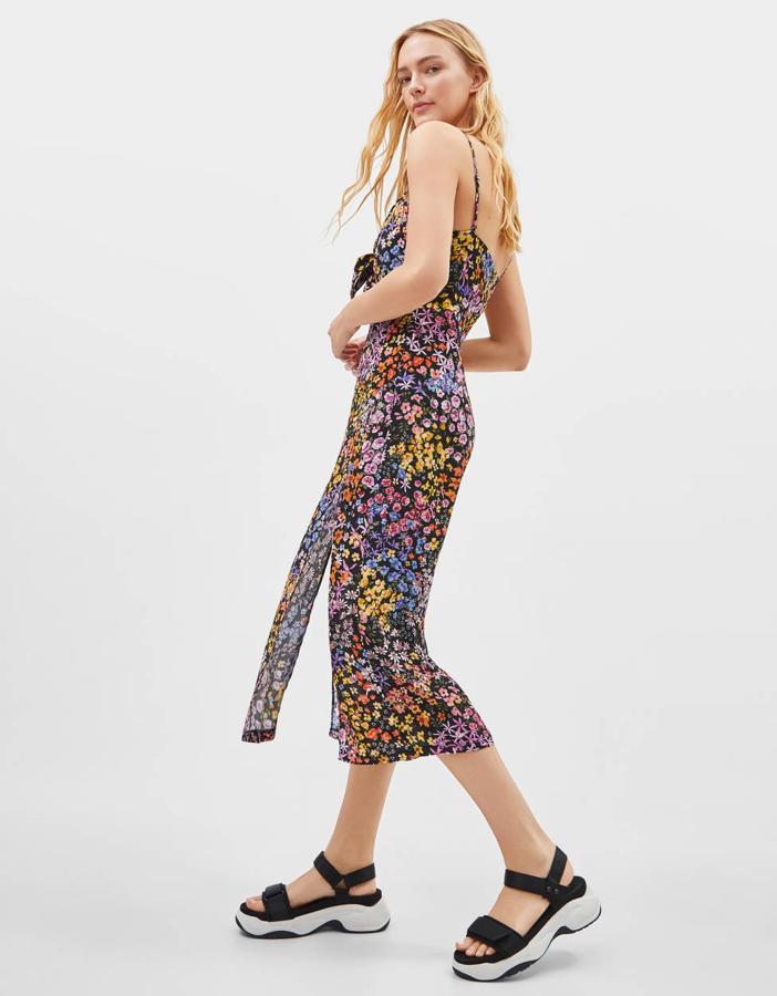 Vestido con unoriginal estampado de pequeñas flores de colores sobre fondo negro de Bershka (29,99 euros). Lleva tirantes, escote recto y una lazada de adorno, además de unas aberturas frontales.