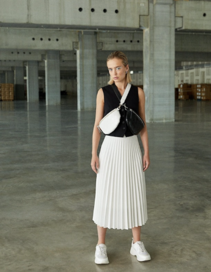 Falda midi plisada con goma en la cintura (25,99 euros), chaleco corto con cierre frontal con botones (17,99 euros) y dos bolsos bandoleras con forma de riñonera cruzados (12,99 euros).