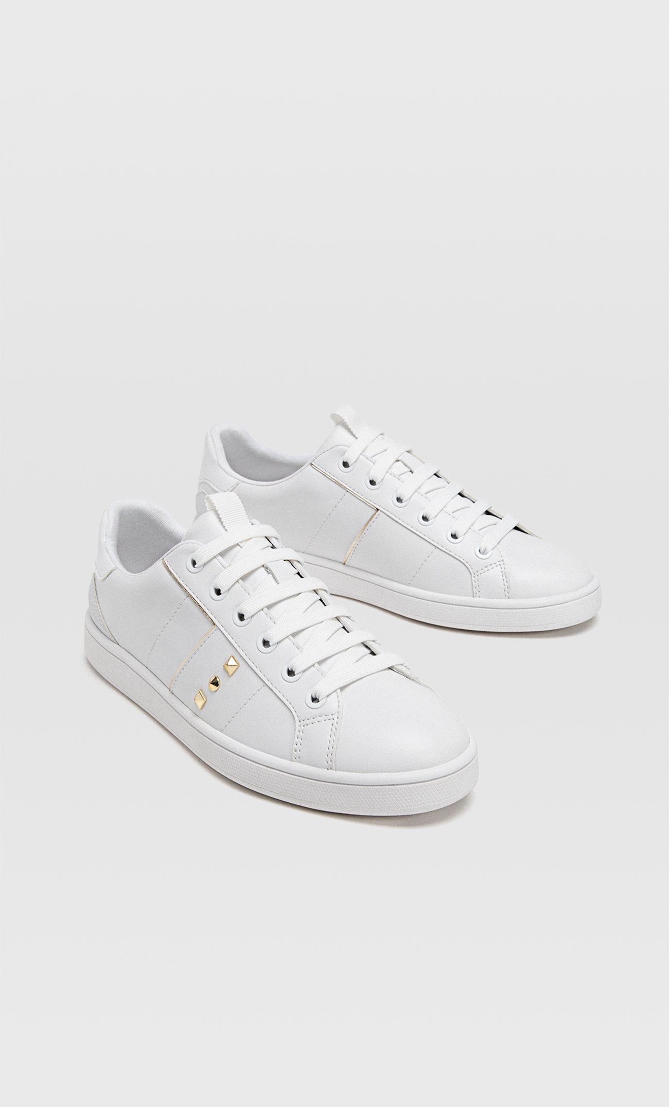 Unas zapatillas blancas para hacer turismo. Estas con detalle de tachuelas son de Stradivarius (19.99 euros).