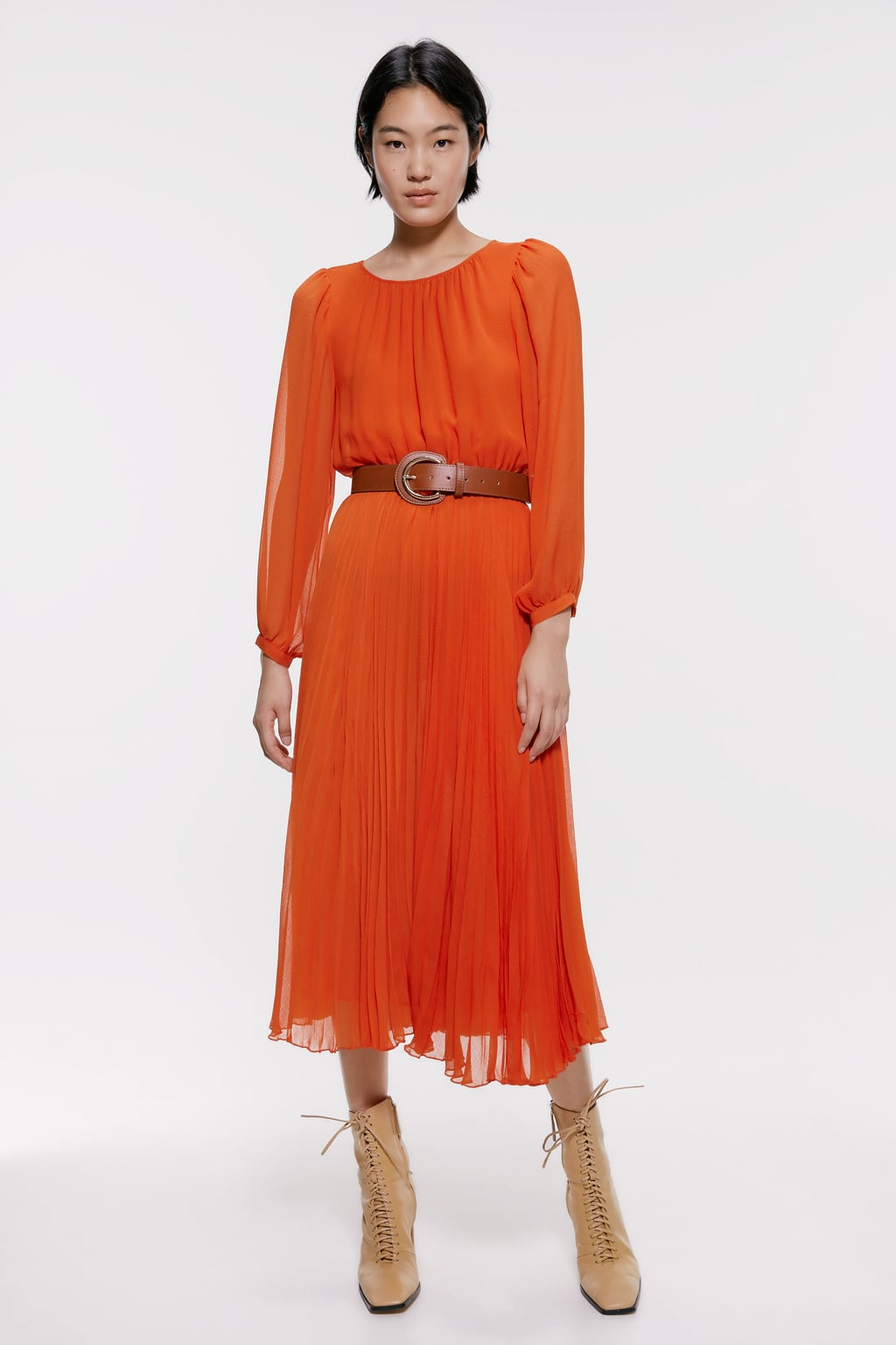 Vestido plisado en tono naranja combinado con cinturón marrón tipo cowboy. Ideal para looks de invitada o para ir al trabajo. (59,95 euros).