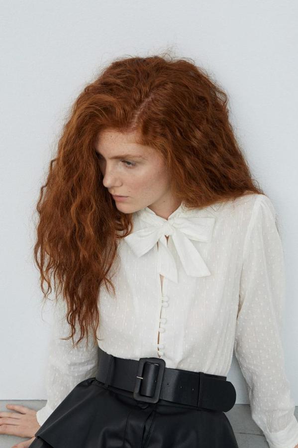 Blusa fluida en tejido bordado, adornada con un lazo corto y una botonadura con dobles botones (Sfera, 19,99 euros).